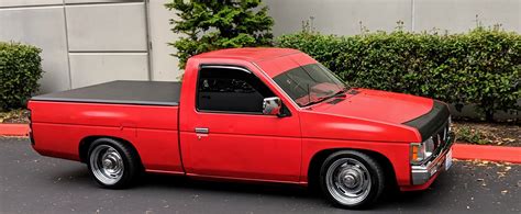 a red pick up truck parked in front of a building next to bushes and trees