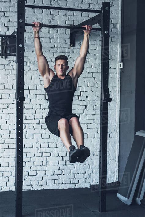 Young man in sportswear doing pull ups on pull up bar in gym - Stock Photo - Dissolve