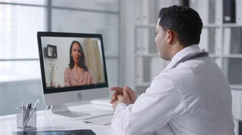 Doctor sitting at desk in front of computer monitor watching his female ...