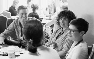 Black and white image of people chatting around a conference table ...