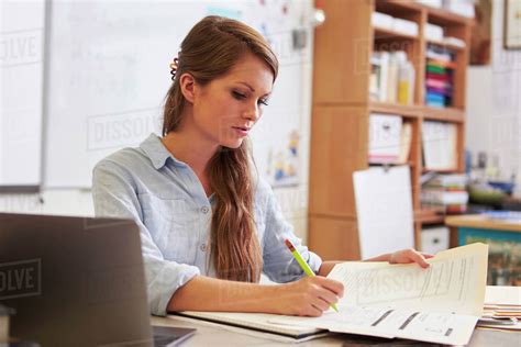 Young female teacher at her desk marking students’ work - Stock Photo - Dissolve