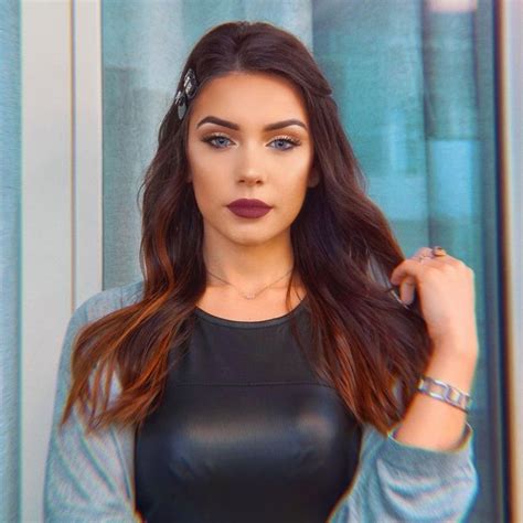 a woman with long brown hair wearing a black top and silver bracelets standing in front of a window