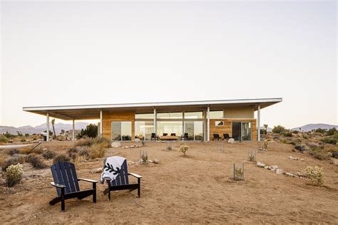 two lawn chairs sitting in front of a house on top of a dirt field next to a desert