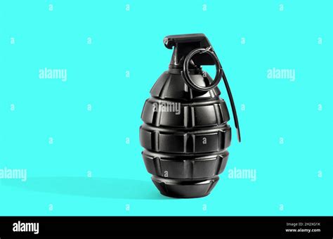 Single unexploded black metal grenade with round pin over cyan background with long shadow and ...
