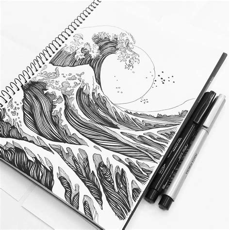 a spiral notebook with an ink drawing of a wave on it and two pens next to it