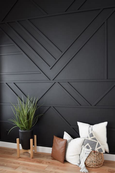 a black wall with some pillows and plants on the floor in front of it, along with two wooden stools