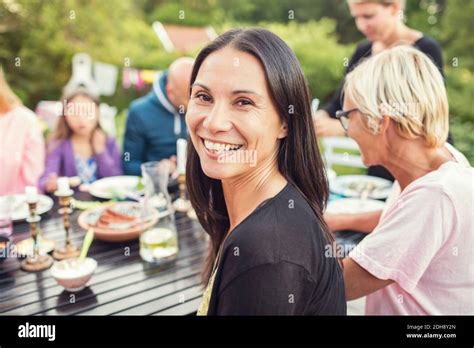 Portrait of happy woman sitting with family and friends at dining table in back yard during ...