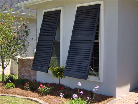 two windows with black shutters on the side of a house in front of flowers