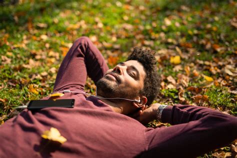 Relaxed young man laying on ground and listening to music on autumn day ...