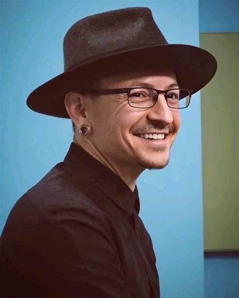 a man wearing glasses and a black hat smiles at the camera while standing in front of a blue wall