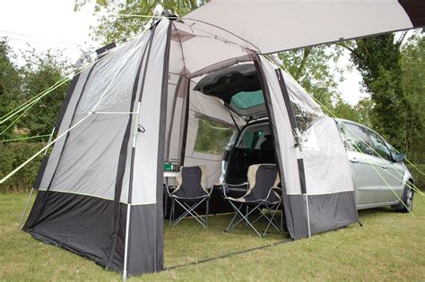 a tent set up in the grass with two chairs and a car parked next to it