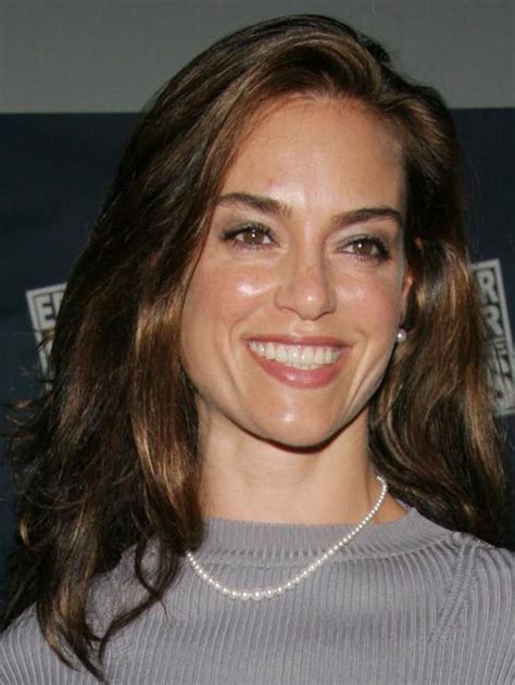 a woman with long hair smiling at the camera while wearing a gray sweater and pearl necklace