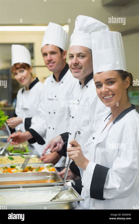 Four chefs working at serving trays smiling at camera Stock Photo - Alamy