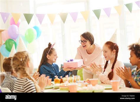 Portrait of excited little girl receiving gifts during Birthday party with friends, copy space ...