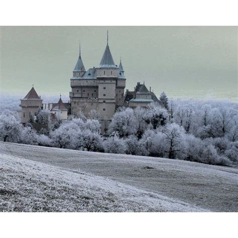 an old castle is surrounded by trees and frosted grass in the foreground,