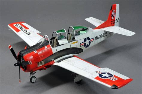 a small red and white airplane on a gray surface with the pilot in the cockpit