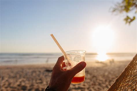 «A Hand Holding A Drink On The Beach.» del colaborador de Stocksy «Denni Van Huis» - Stocksy