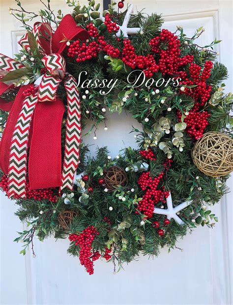 a christmas wreath with red berries and white starfishs on it, hanging from the side of a door