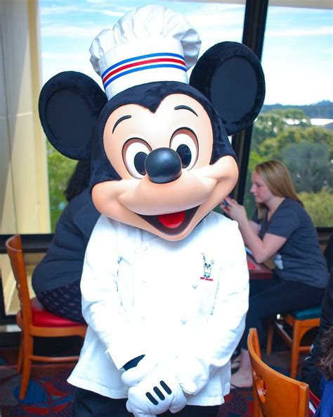 a person in a mickey mouse costume standing next to a table with people sitting at tables