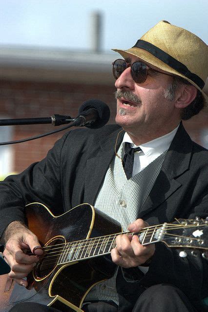 a man in a suit and hat playing an acoustic guitar