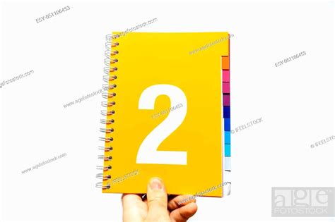 Male hand holding notebook with big number 2 printed on orange yellow color ready for ...
