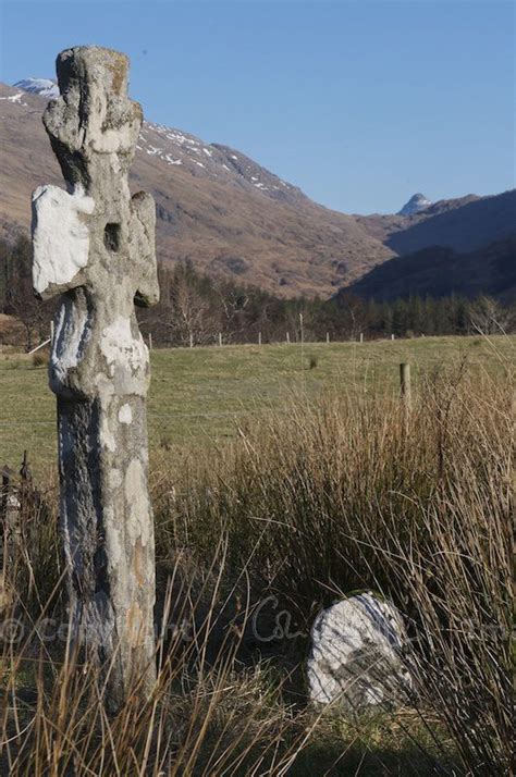 an old stone cross in the middle of a grassy field with mountains in the background