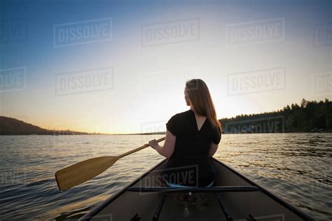 A young woman canoeing at sunset; Vancouver, British Columbia, Canada ...