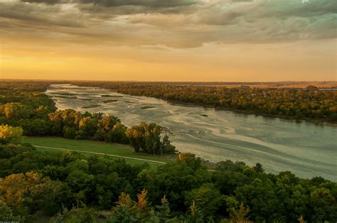 an aerial view of a river with trees in the foreground and clouds in ...