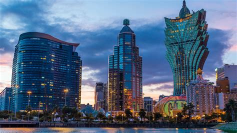 some very tall buildings by the water at sunset or dawn with lights reflecting off them