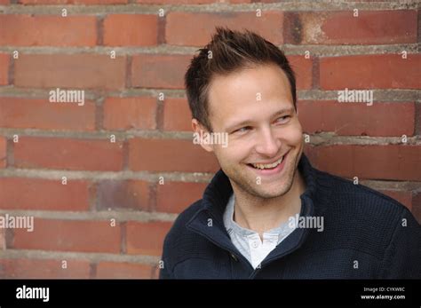 Smiling man leaning against brick wall Stock Photo - Alamy