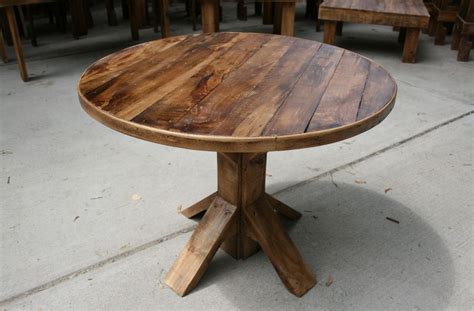 a round wooden table sitting on top of a cement floor next to tables and chairs