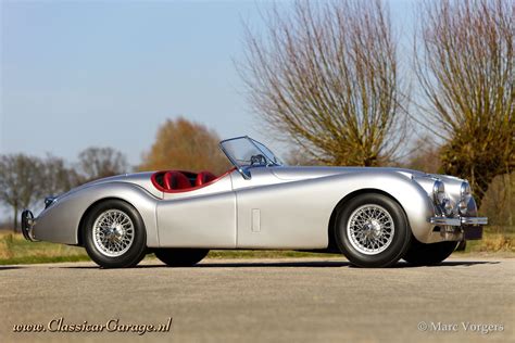 an old silver sports car parked on the side of the road in front of ...