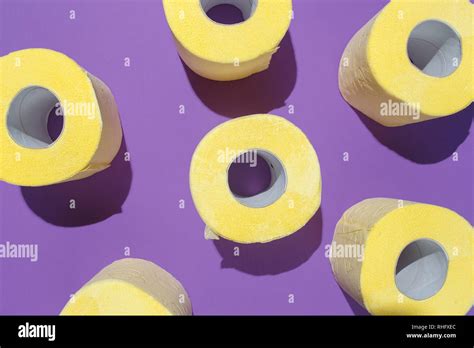 Pattern of bright yellow toilet paper rolls on purple background. Flat composition, top view ...