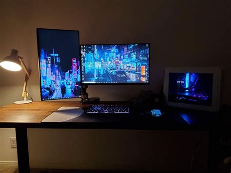 two computer monitors sitting next to each other on a desk in front of a lamp