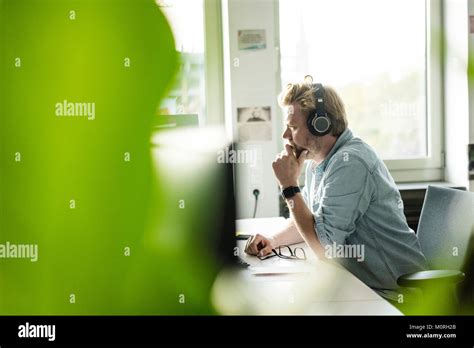 Businessman wearing headphones at desk in office Stock Photo - Alamy