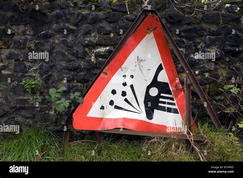 Damaged road warning sign against a stone wall in the village of Castle ...