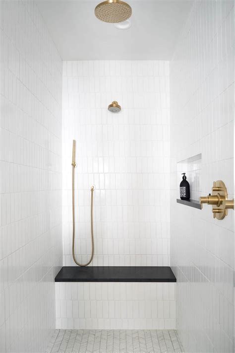 a white tiled bathroom with gold fixtures and black countertop, along ...