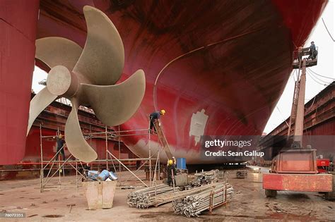 Workers finish maintenance work on a cargo ship's propeller as other ...