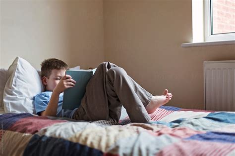 "Boy Reading A Book While Lying On A Bed" by Stocksy Contributor "Kirsty Begg" - Stocksy