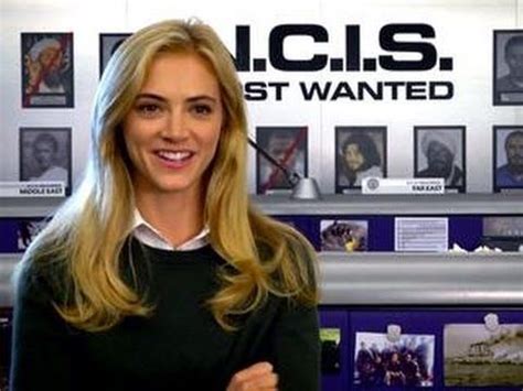 a woman standing in front of a wall with pictures on it's walls and smiling at the camera