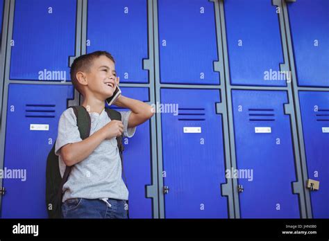 Happy boy talking on mobile phone while standing against lockers at school Stock Photo - Alamy