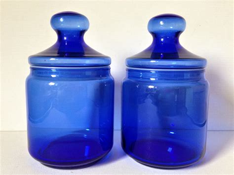 two blue glass jars with lids sitting on a white counter top next to each other