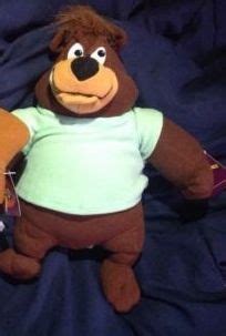 a stuffed bear with a green shirt on it's chest and legs, sitting on a blue sheet