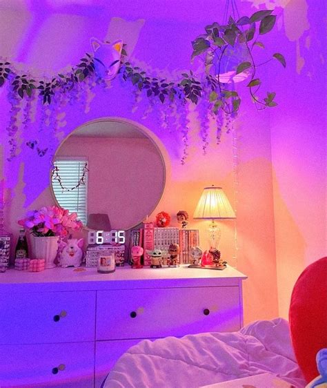 a bedroom decorated in pink and purple with flowers on the dresser, mirror and lamp