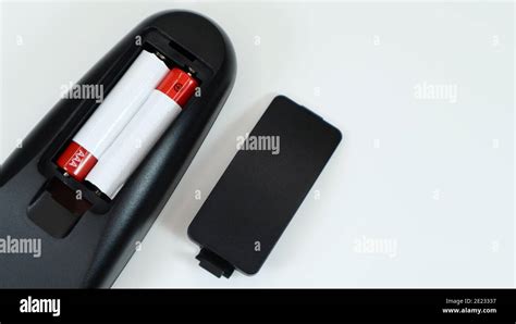 Black TV remote control with AAA alkaline batteries in red and white on a white background ...