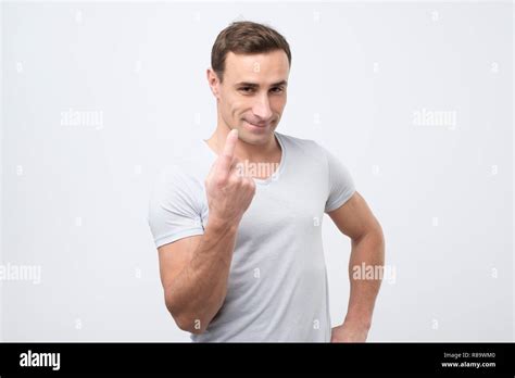 Handsome young man showing come here gesture with index finger and smiling over gray background ...