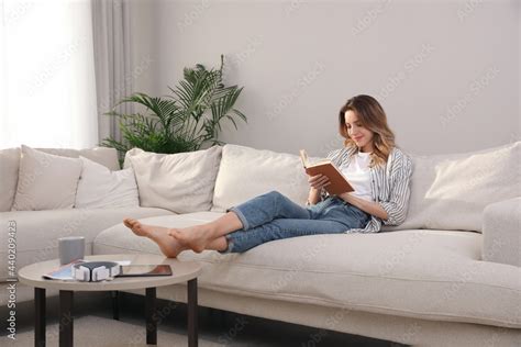 Young woman reading book on sofa at home Stock Photo | Adobe Stock