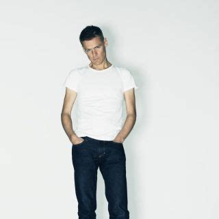 a man standing in front of a white wall wearing jeans and a t - shirt