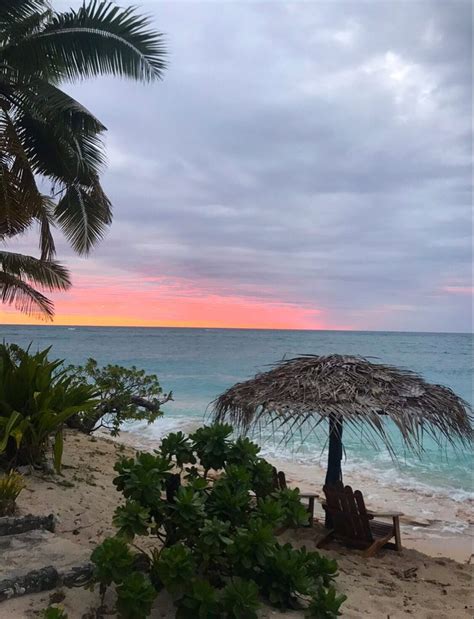 an umbrella and chairs on the beach at sunset with palm trees in the ...