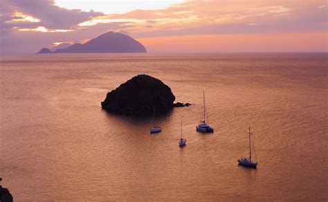 several sailboats in the water at sunset with an island in the middle of the ocean